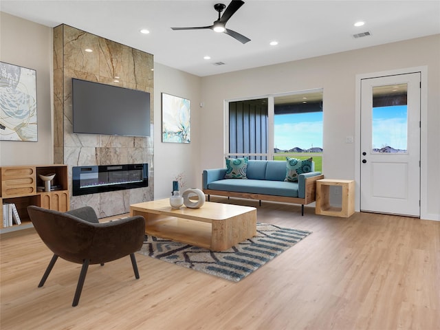 living room featuring ceiling fan, light hardwood / wood-style flooring, and a fireplace