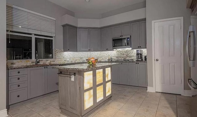 kitchen featuring light stone counters, a center island, refrigerator, and gray cabinetry