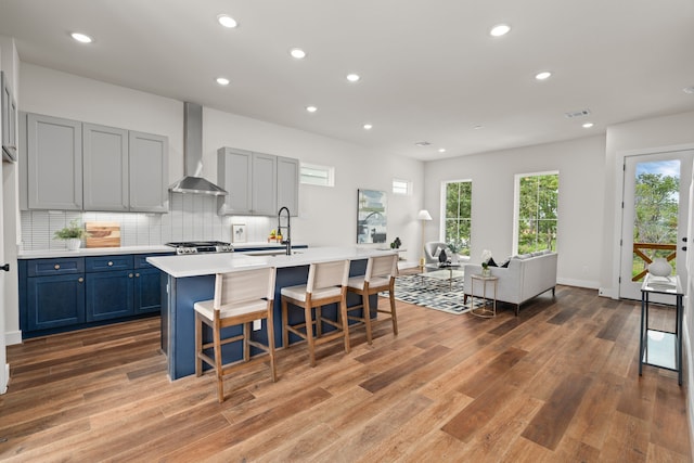 kitchen with a center island with sink, a breakfast bar, sink, hardwood / wood-style flooring, and wall chimney exhaust hood