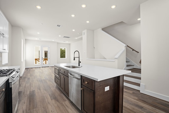 kitchen with appliances with stainless steel finishes, a kitchen island with sink, dark wood-type flooring, white cabinets, and sink