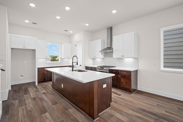 kitchen with dark hardwood / wood-style floors, sink, an island with sink, wall chimney exhaust hood, and gas range