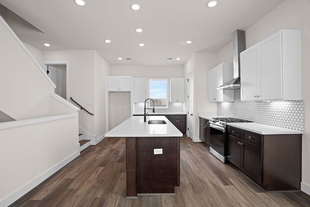 kitchen featuring wall chimney range hood, a center island with sink, stainless steel gas range oven, sink, and dark wood-type flooring