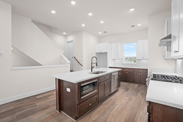 kitchen with exhaust hood, black microwave, sink, stainless steel dishwasher, and a center island with sink