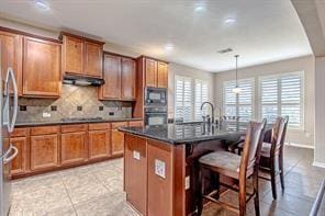 kitchen with tasteful backsplash, decorative light fixtures, a kitchen island with sink, a breakfast bar, and black appliances