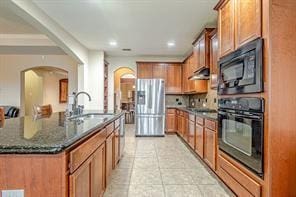 kitchen featuring black appliances, sink, light tile patterned flooring, an island with sink, and dark stone counters