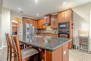 kitchen featuring black appliances, dark stone counters, an island with sink, sink, and a breakfast bar area