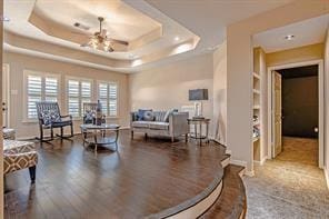 living room with hardwood / wood-style flooring, ceiling fan, built in features, and a raised ceiling