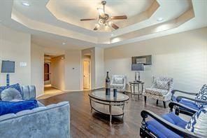 living room with ceiling fan, dark hardwood / wood-style floors, and a tray ceiling