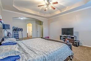 bedroom with a raised ceiling, ceiling fan, carpet, and crown molding