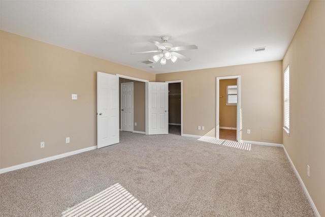 unfurnished bedroom with ceiling fan, light carpet, a closet, and a walk in closet