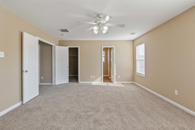 unfurnished bedroom with a spacious closet, connected bathroom, a closet, ceiling fan, and light colored carpet