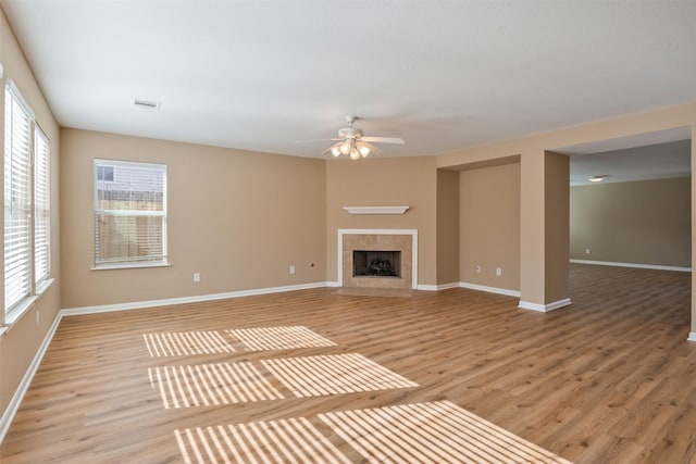 unfurnished living room with ceiling fan, a tiled fireplace, and light hardwood / wood-style flooring