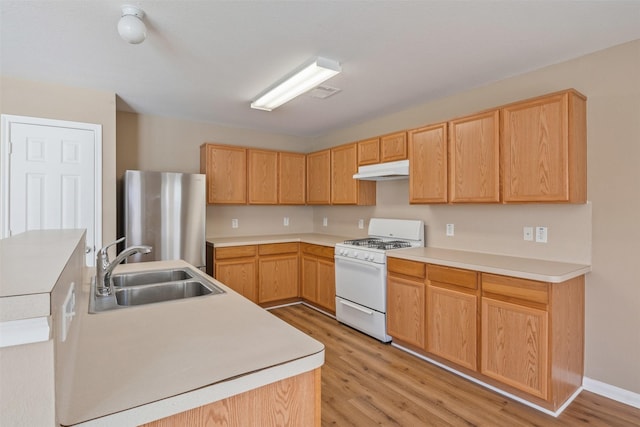 kitchen with gas range gas stove, light hardwood / wood-style floors, light brown cabinets, stainless steel refrigerator, and sink