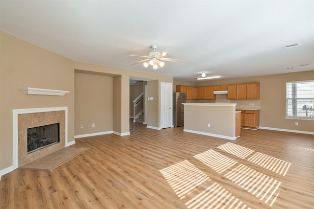 unfurnished living room featuring ceiling fan, a tile fireplace, and light hardwood / wood-style floors