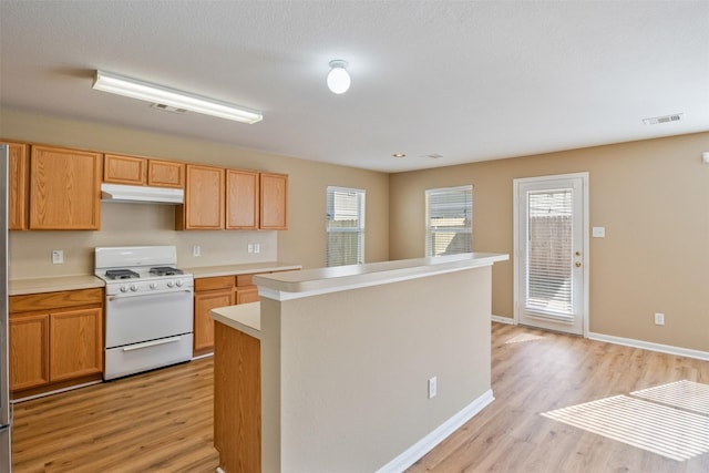 kitchen featuring white range with gas stovetop, a wealth of natural light, light hardwood / wood-style flooring, and a center island