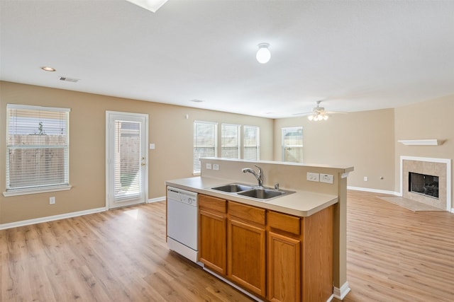 kitchen featuring dishwasher, light hardwood / wood-style floors, sink, a tile fireplace, and a center island with sink