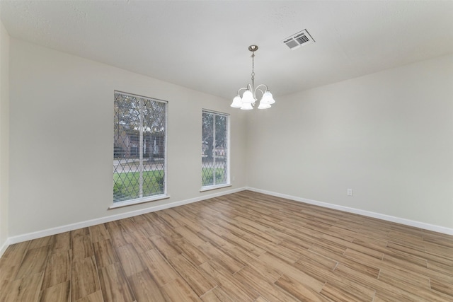 unfurnished room featuring a notable chandelier and light hardwood / wood-style flooring