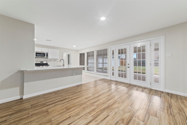 unfurnished living room with light hardwood / wood-style flooring, sink, a wealth of natural light, and french doors