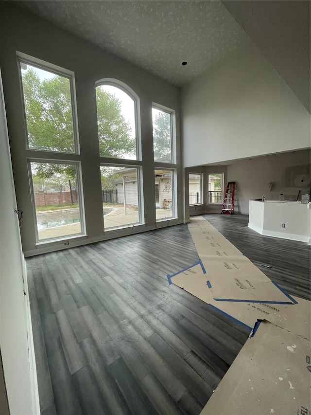 empty room featuring a textured ceiling, dark hardwood / wood-style flooring, and a towering ceiling