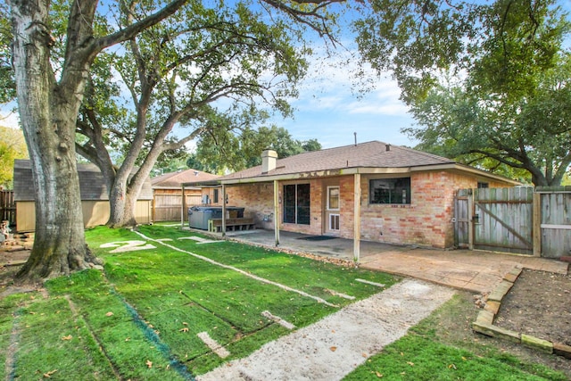 back of property featuring a hot tub, a patio area, and a yard