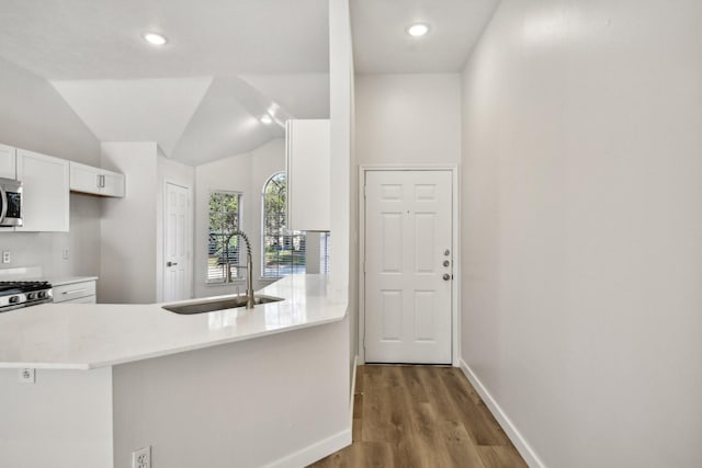 kitchen with white cabinets, lofted ceiling, wood-type flooring, sink, and kitchen peninsula