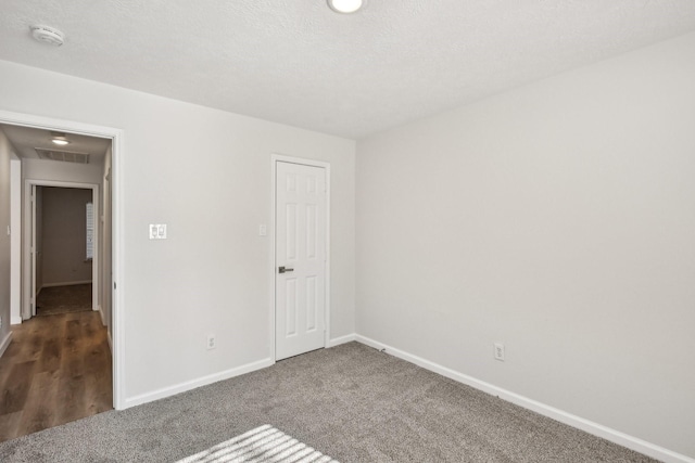 unfurnished room with a textured ceiling and dark colored carpet