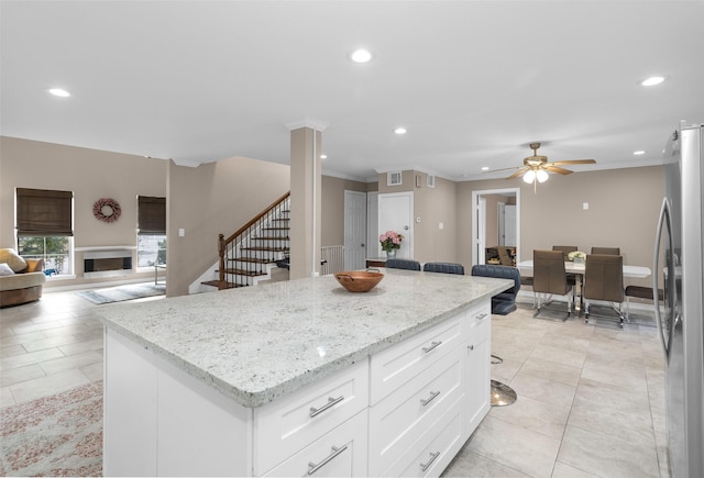 kitchen featuring white cabinetry, stainless steel fridge, a kitchen island, ceiling fan, and light stone countertops