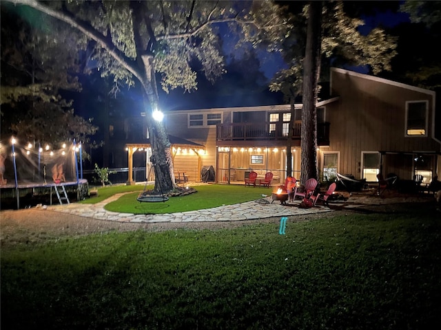 back house at night with a balcony, a yard, and a trampoline