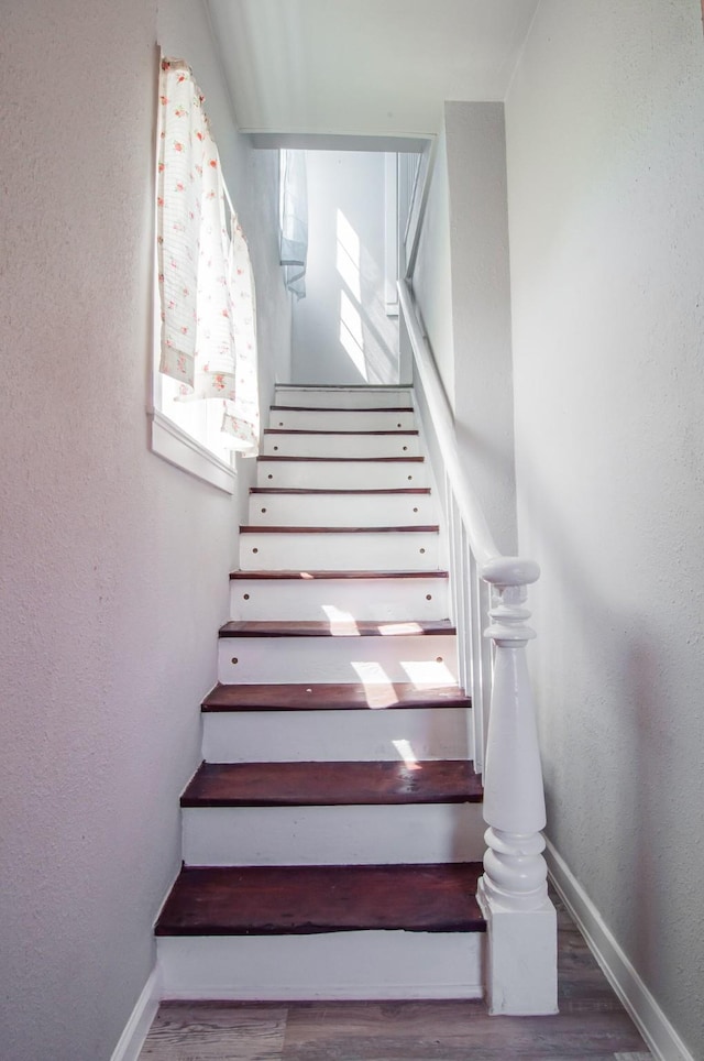 stairs with a textured wall, baseboards, and wood finished floors