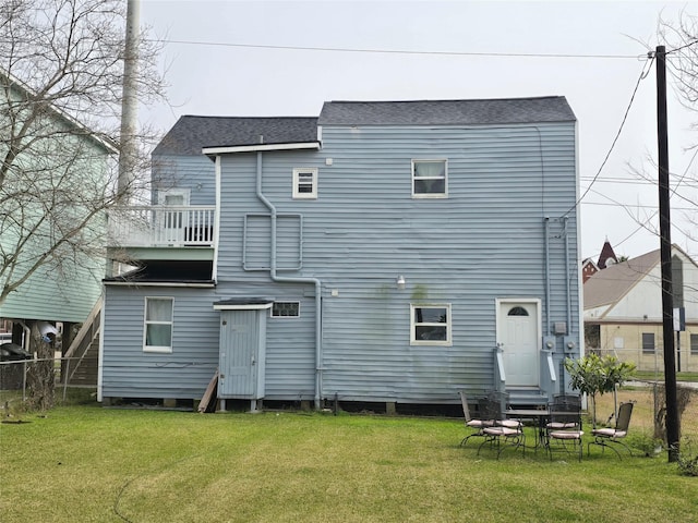 rear view of house with a lawn, fence, and roof with shingles