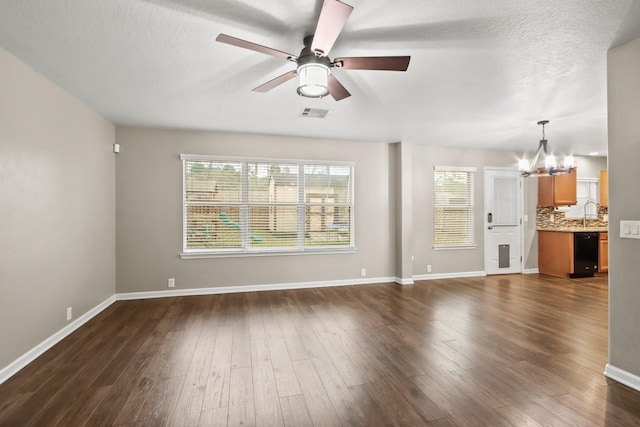 unfurnished living room featuring ceiling fan with notable chandelier, dark wood-type flooring, and a textured ceiling