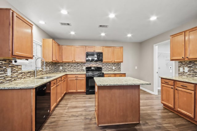 kitchen with light stone countertops, black appliances, a kitchen island, wood-type flooring, and sink