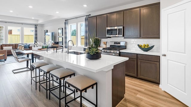 kitchen featuring a breakfast bar area, tasteful backsplash, appliances with stainless steel finishes, a kitchen island with sink, and a sink