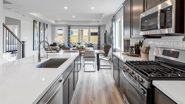 kitchen featuring a tray ceiling, stainless steel appliances, tasteful backsplash, light countertops, and a sink