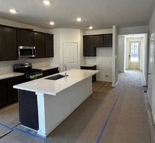 kitchen with a center island with sink, appliances with stainless steel finishes, a sink, light countertops, and backsplash