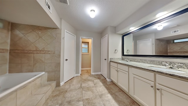 bathroom featuring tiled bath, vanity, and a textured ceiling