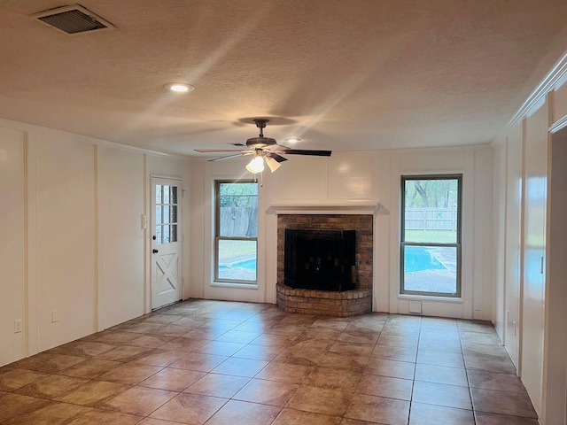 unfurnished living room with ceiling fan, a textured ceiling, a healthy amount of sunlight, and a fireplace