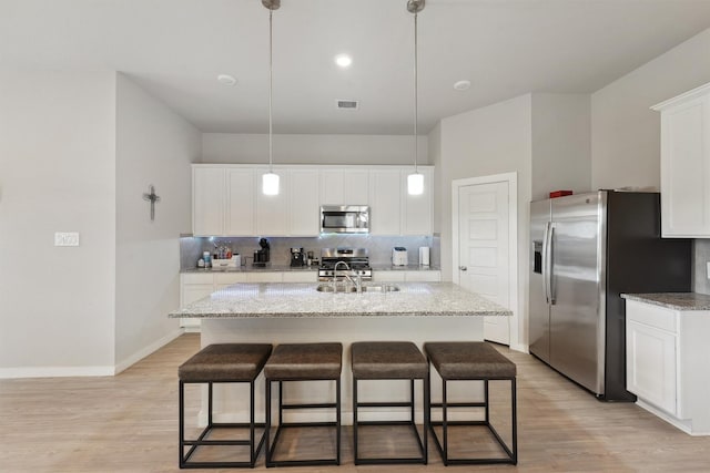 kitchen featuring white cabinetry, light hardwood / wood-style flooring, hanging light fixtures, a kitchen island with sink, and stainless steel appliances