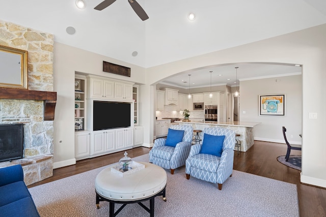 living room featuring ceiling fan, dark hardwood / wood-style flooring, crown molding, and a fireplace