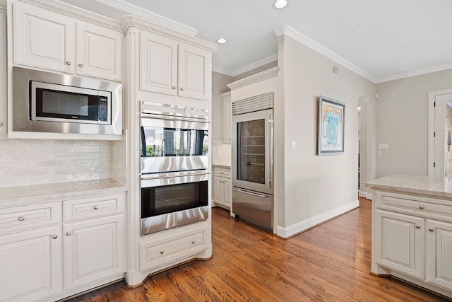 kitchen featuring decorative backsplash, crown molding, stainless steel appliances, and white cabinetry