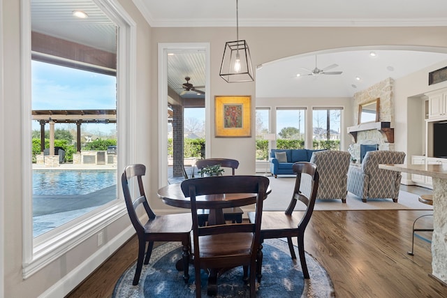 dining area with ceiling fan, a stone fireplace, ornamental molding, and hardwood / wood-style floors