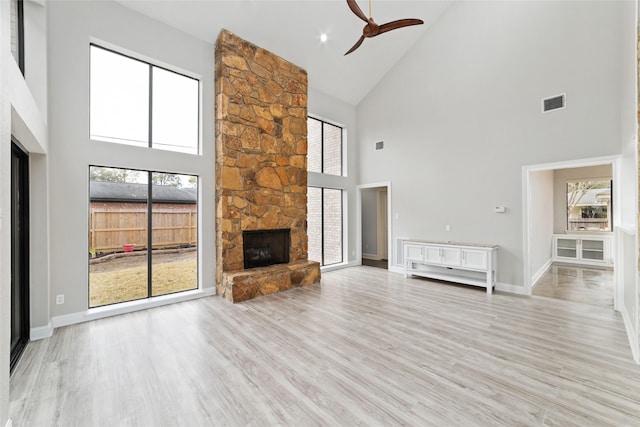 unfurnished living room with high vaulted ceiling, ceiling fan, a fireplace, and light wood-type flooring