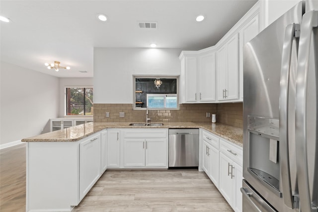 kitchen featuring light stone countertops, white cabinetry, stainless steel appliances, sink, and kitchen peninsula