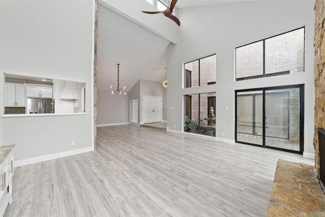 unfurnished living room featuring high vaulted ceiling, ceiling fan with notable chandelier, and light hardwood / wood-style floors