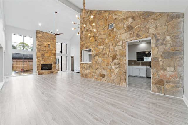 unfurnished living room featuring a fireplace, beam ceiling, an inviting chandelier, light hardwood / wood-style flooring, and high vaulted ceiling