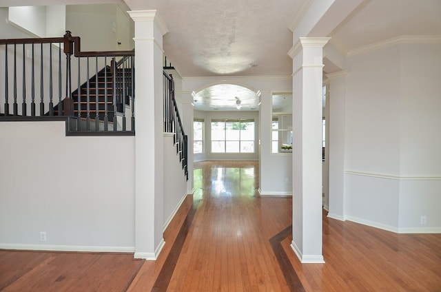 hall with hardwood / wood-style flooring, a textured ceiling, decorative columns, and ornamental molding