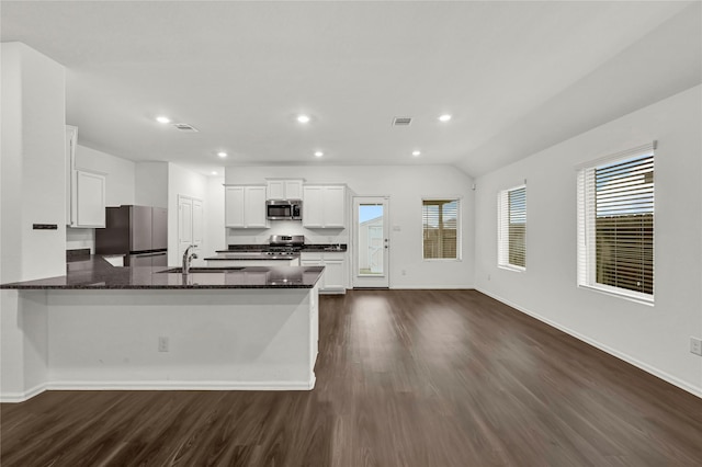 kitchen with appliances with stainless steel finishes, dark wood-type flooring, white cabinetry, dark stone countertops, and sink