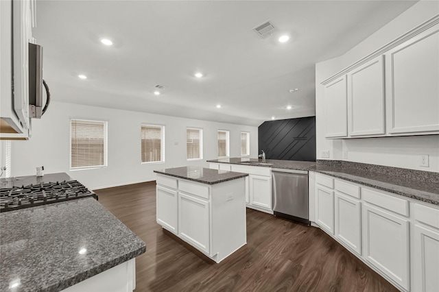 kitchen with white cabinetry, stainless steel appliances, a center island, dark stone countertops, and sink