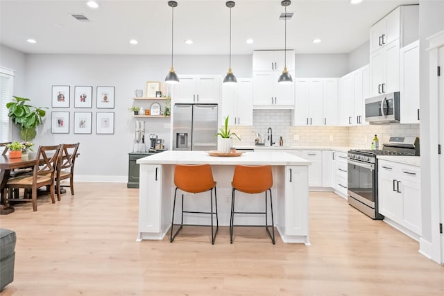 kitchen featuring hanging light fixtures, stainless steel appliances, white cabinets, and a kitchen island