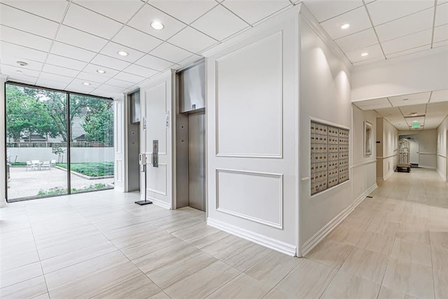 corridor featuring a paneled ceiling, elevator, a mail area, and expansive windows